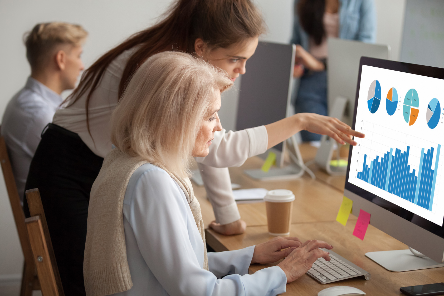 Young executive teaching older colleague explaining digital statistics data analysis